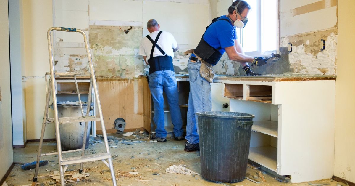 Technician using gloves and chemical solutions to remove adhesive residue from walls during a renovation project.