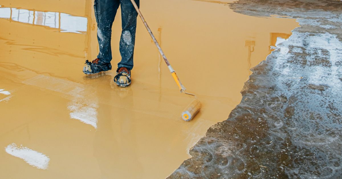 Workers applying epoxy floor coating in an industrial warehouse using rollers and squeegees.